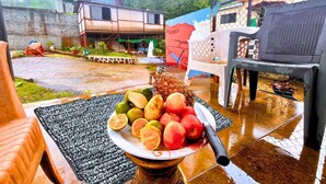Een rustieke buitenzitplek met een tafel waarop een schaal fruit staat, een overdekte zithoek en een gebouw met de tekst 