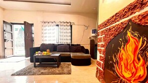 Een ruime woonkamer met een zithoek, een bijzettafeltje met fruit, en een groot schilderij aan de muur.