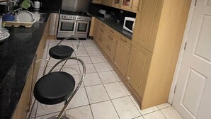 A kitchen with wooden cabinets, a stove, an oven, and a microwave. There are three bar stools and a sink.