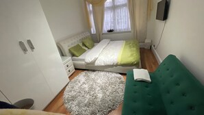 A bedroom with a bed, a green sofa, a white fluffy rug, and a window with curtains.