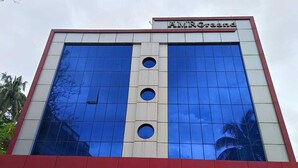 A modern building with a reflective glass facade, a prominent AMRO Grand sign, and a red and white color scheme. - Hotel AMR GRAND (Port Blair)