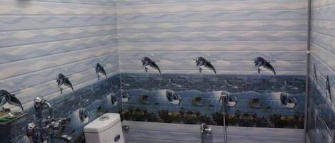 A bathroom with a tiled wall featuring a marine life mural, a toilet, and a shower area.