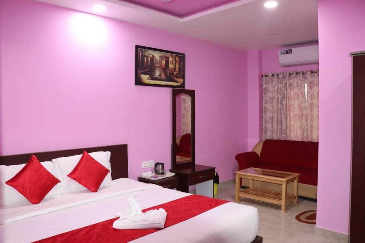 A hotel room with a bed, a red sofa, a small table, a mirror, and an air conditioning unit.