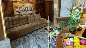 A modern living room with a sofa, a decorative wall, a table with a plant, and a brass lamp. - Hotel AMR GRAND (Port Blair)