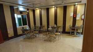 A conference room with multiple tables and chairs, a polished marble floor, and a window with a view. - Hotel AMR GRAND (Port Blair)