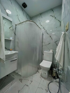 Un baño con suelo de mármol, cabina de ducha, inodoro y lavabo con espejo.
