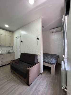 Un espacio habitable compacto con sofá, cama, kitchenette y equipo de aire acondicionado.