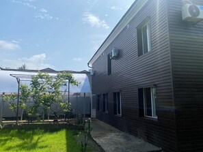 Un edificio residencial con fachada oscura, un patio cubierto y un jardín con césped.