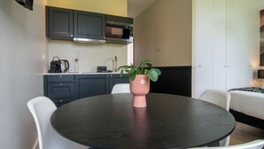 A compact kitchen with dark cabinets, a black countertop, and a round table with a potted plant. - Amélia - Apartment 3★ - 4 pers - Near Etretat - Parking - High Speed Wifi (La Poterie-Cap-d'Antifer)