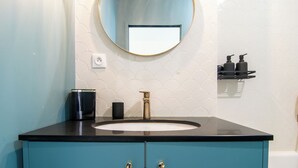 A bathroom with a teal vanity, a round mirror, and a white tiled wall. - Amélia - Apartment 3★ - 4 pers - Near Etretat - Parking - High Speed Wifi (La Poterie-Cap-d'Antifer)