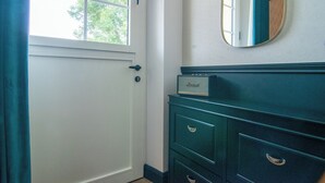 A room with a white door, a window with a view of trees, a dark blue dresser with drawers, and a mirror on the wall. - Amélia - Apartment 3★ - 4 pers - Near Etretat - Parking - High Speed Wifi (La Poterie-Cap-d'Antifer)