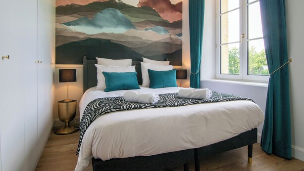 A neatly made bed with white and teal bedding, a large abstract mural on the wall, and a window with teal curtains. - Amélia - Apartment 3★ - 4 pers - Near Etretat - Parking - High Speed Wifi (La Poterie-Cap-d'Antifer)