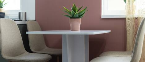 A dining area with a white table, two beige chairs, and a potted plant on the table.