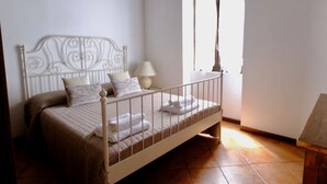 Ein Einzelbett mit Metallkopfteil, einer Nachttischlampe und einem Fenster mit Vorhängen.