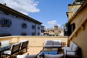 A rooftop terrace with outdoor furniture, a glass table, and a view of historic buildings.