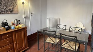 Ein Essbereich mit einem Glastisch und Stühlen, einem Holzschrank mit Küchenutensilien, einem Heizkörper und einer Tür.
