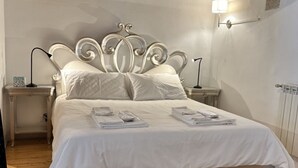 Ein ordentlich bezogenes Bett mit weißen Leinen und Kissen, zwei Nachttische mit Lampen sowie ein kleiner dekorativer Gegenstand.