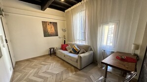Una sala de estar con piso de espiga, un sofá con cojines, una mesa con camino de mesa rojo y un cuadro en la pared.