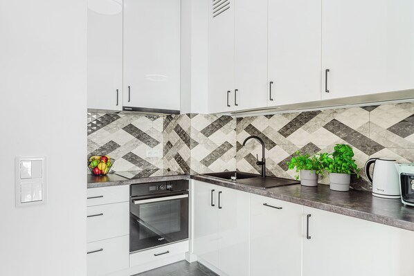 Eine moderne Küche mit weißen Schränken, einem eingebauten Backofen, einer Edelstahl-Spüle und einer gemusterten Spritzschutzwand.