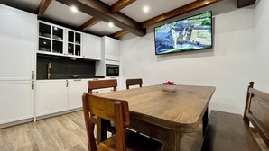Uma cozinha moderna com armários brancos, uma mesa de jantar de madeira e uma televisão fixada na parede.