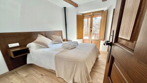 Quarto com cabeceira de madeira, cama com roupa de cama branca, mesa de cabeceira de madeira e uma grande janela com vista para um deck de madeira.