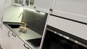 Uma cozinha moderna com armários brancos, bancada preta, torneira dourada e forno embutido.