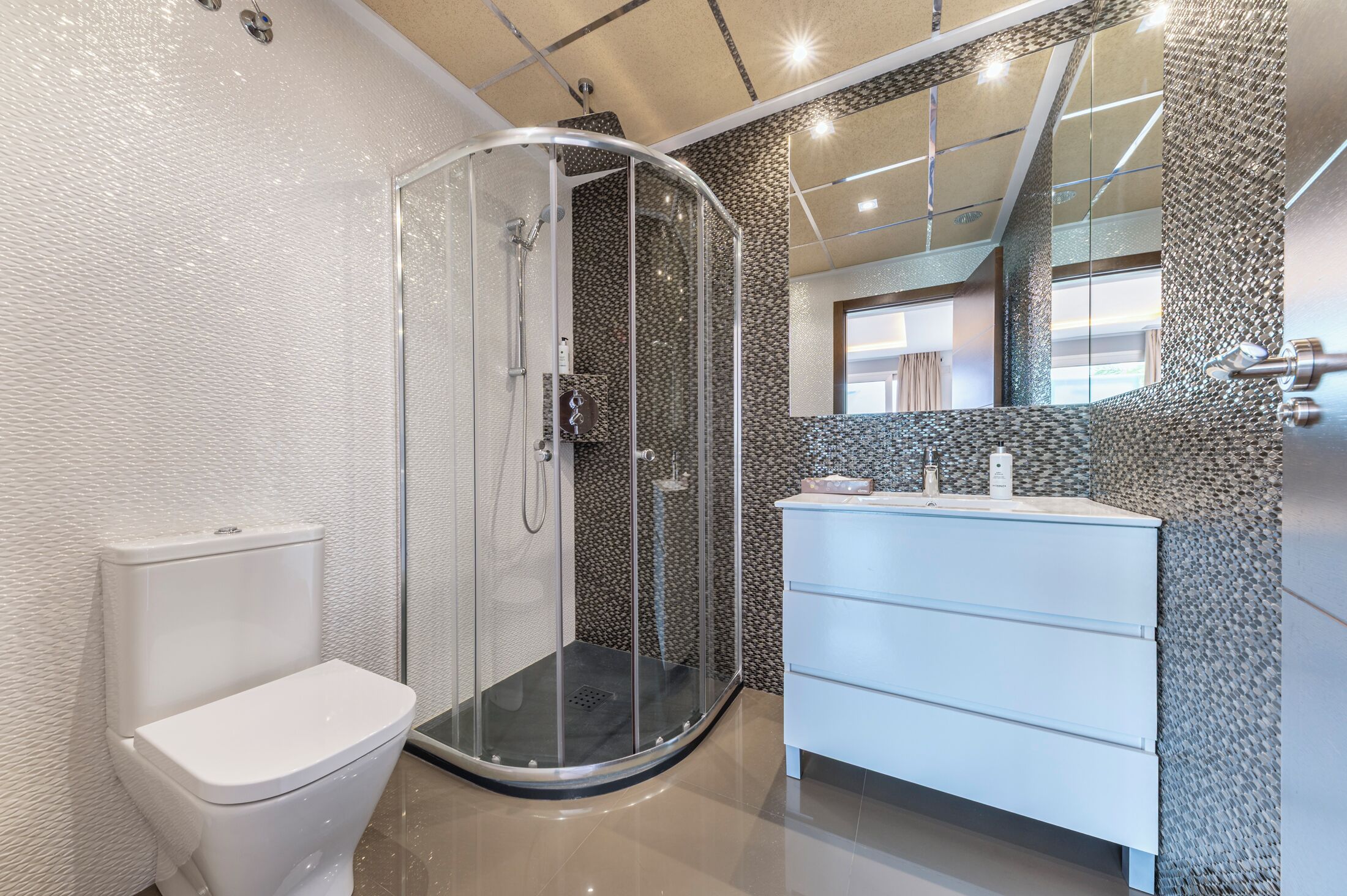 A modern bathroom with a glass-enclosed shower, a white toilet, and a white vanity with a mirror.
