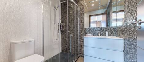 A modern bathroom with a glass-enclosed shower, a white toilet, and a white vanity with a mirror.
