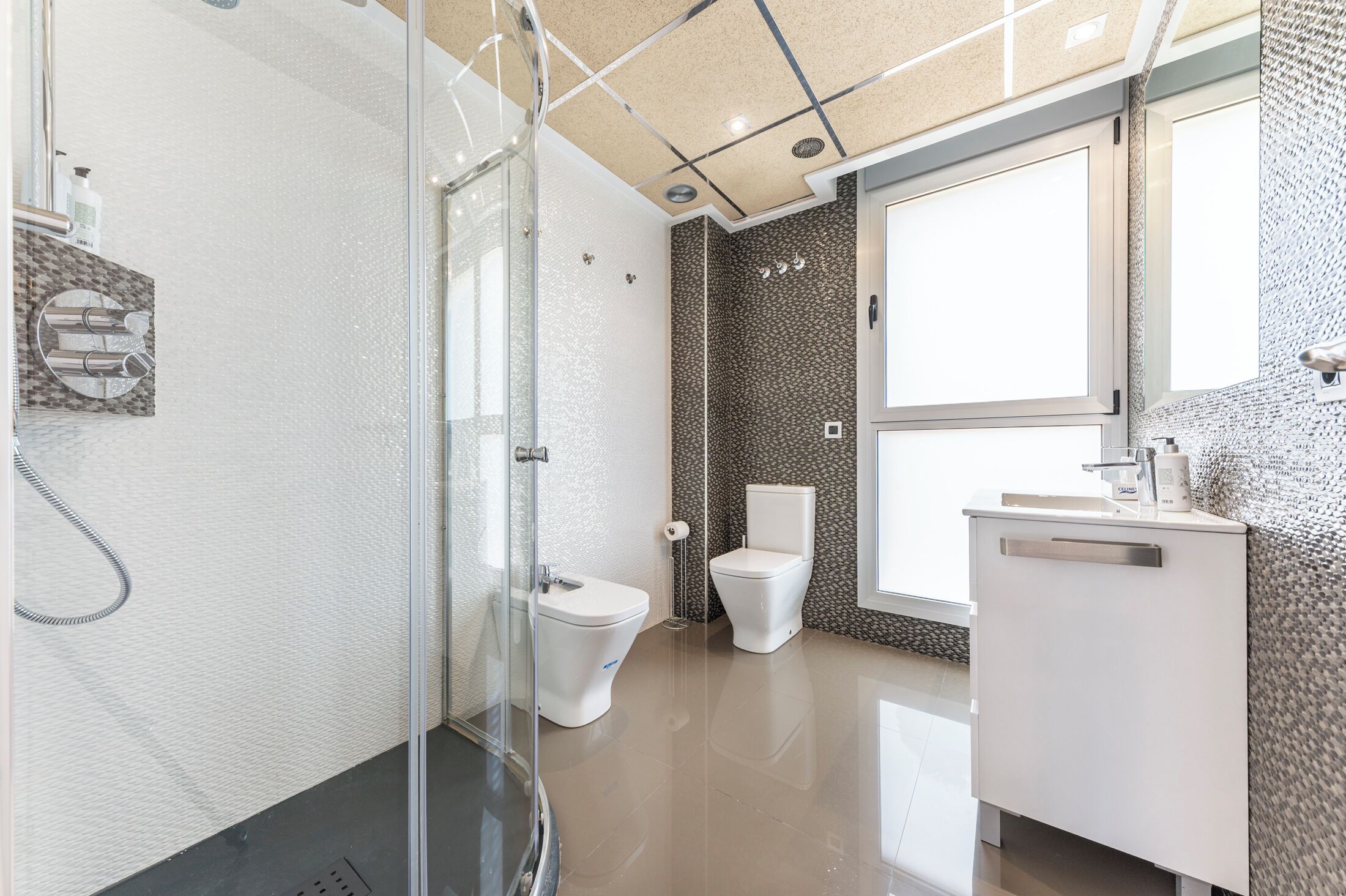 A modern bathroom with a glass shower enclosure, a white toilet, and a white sink with a mirror above it.