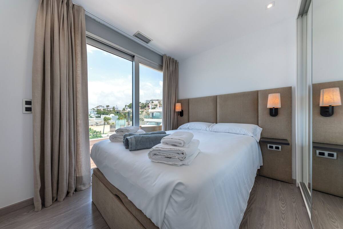 Une chambre d’hôtel moderne avec un grand lit, deux lampes de chevet et une vue sur la ville.