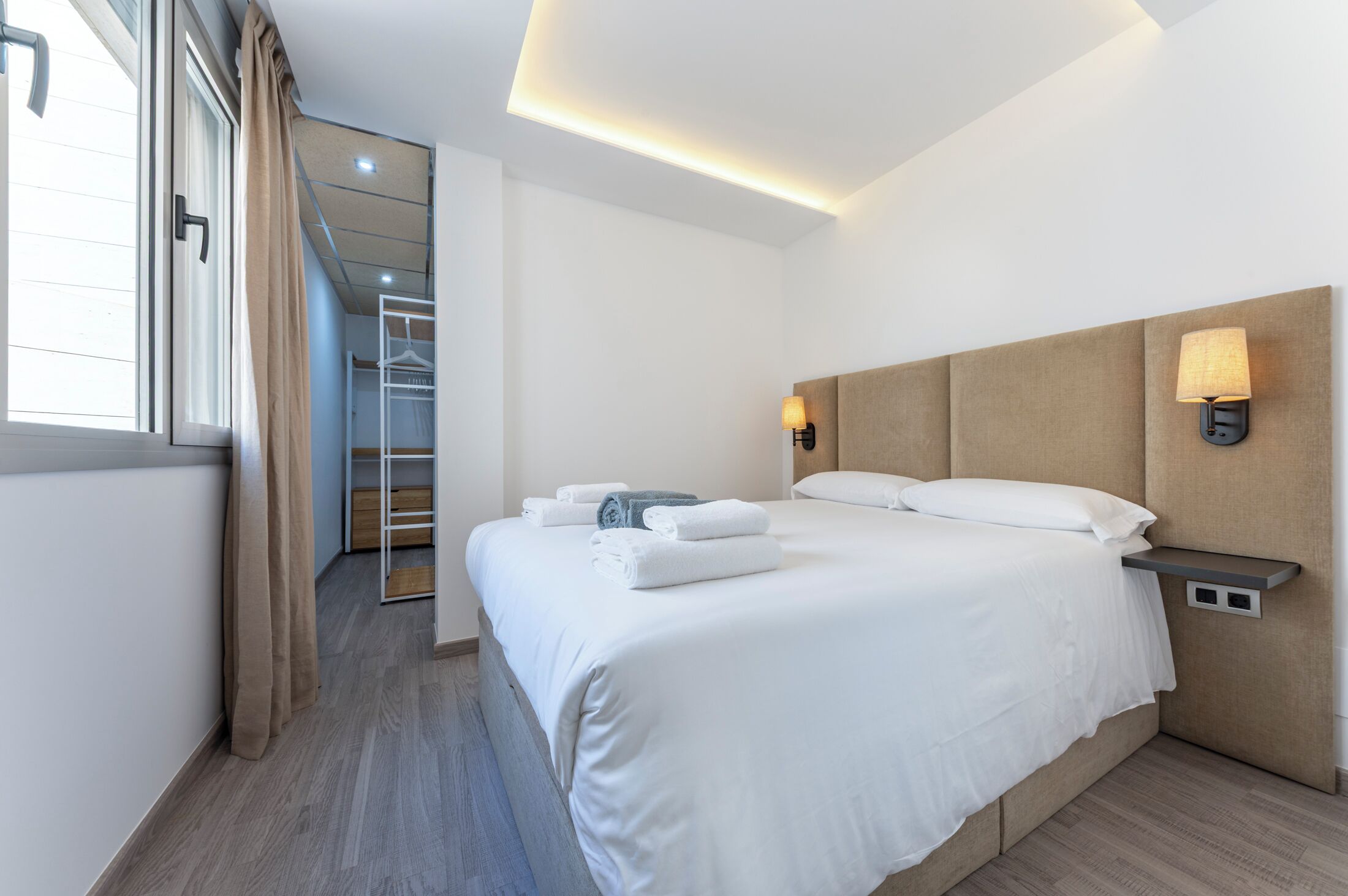 A modern hotel room with a large bed, a bedside table with a lamp, and a view of a walk-in closet.