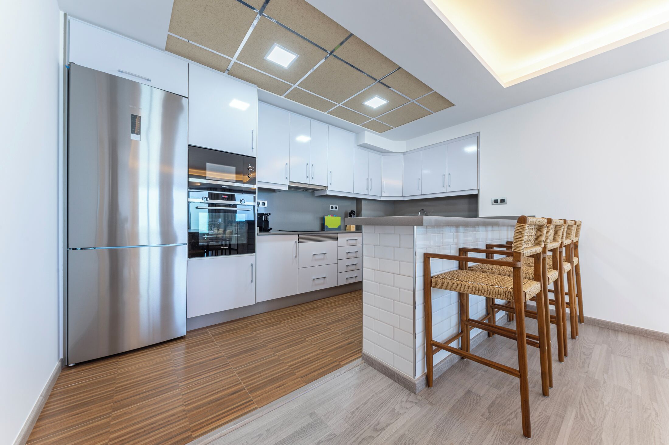 A modern kitchen with white cabinets, stainless steel appliances, and a wooden floor.