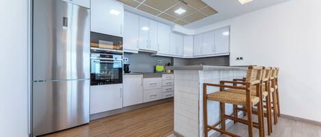 A modern kitchen with white cabinets, stainless steel appliances, and a wooden floor.