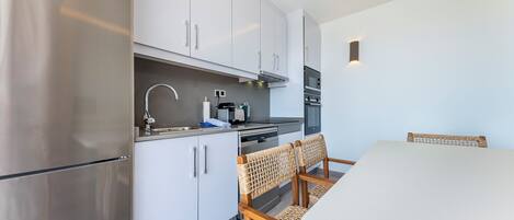 Una cocina moderna con alacenas blancas, electrodomésticos de acero inoxidable y un comedor con sillas de mimbre.