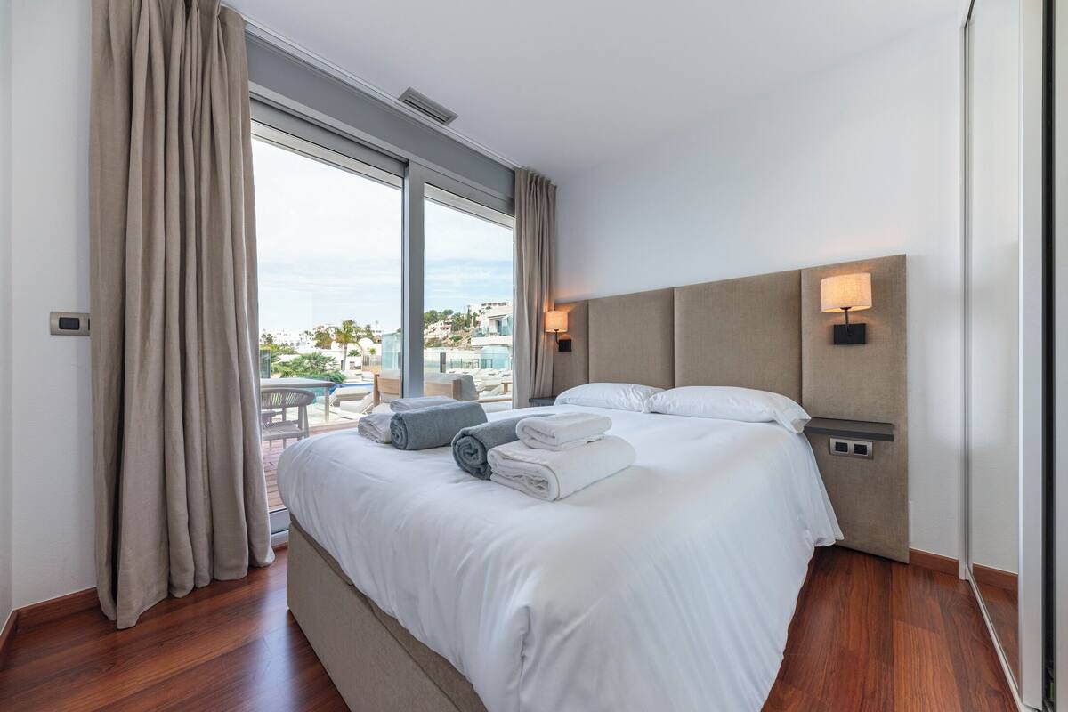 Une chambre d’hôtel avec un grand lit, deux tables de chevet, une fenêtre avec des rideaux et une vue sur la ville.