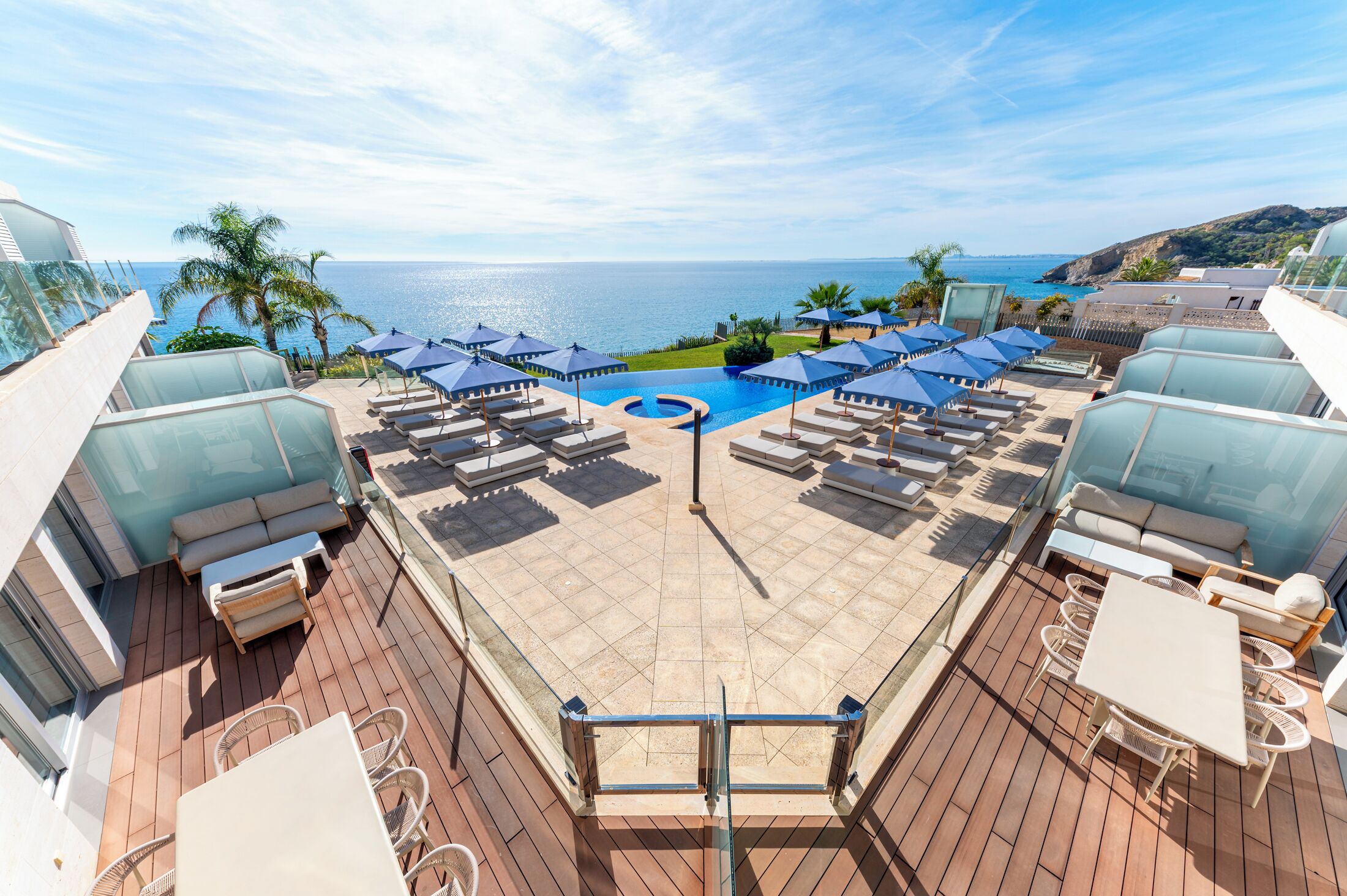 A rooftop pool area with lounge chairs and umbrellas, overlooking the sea.