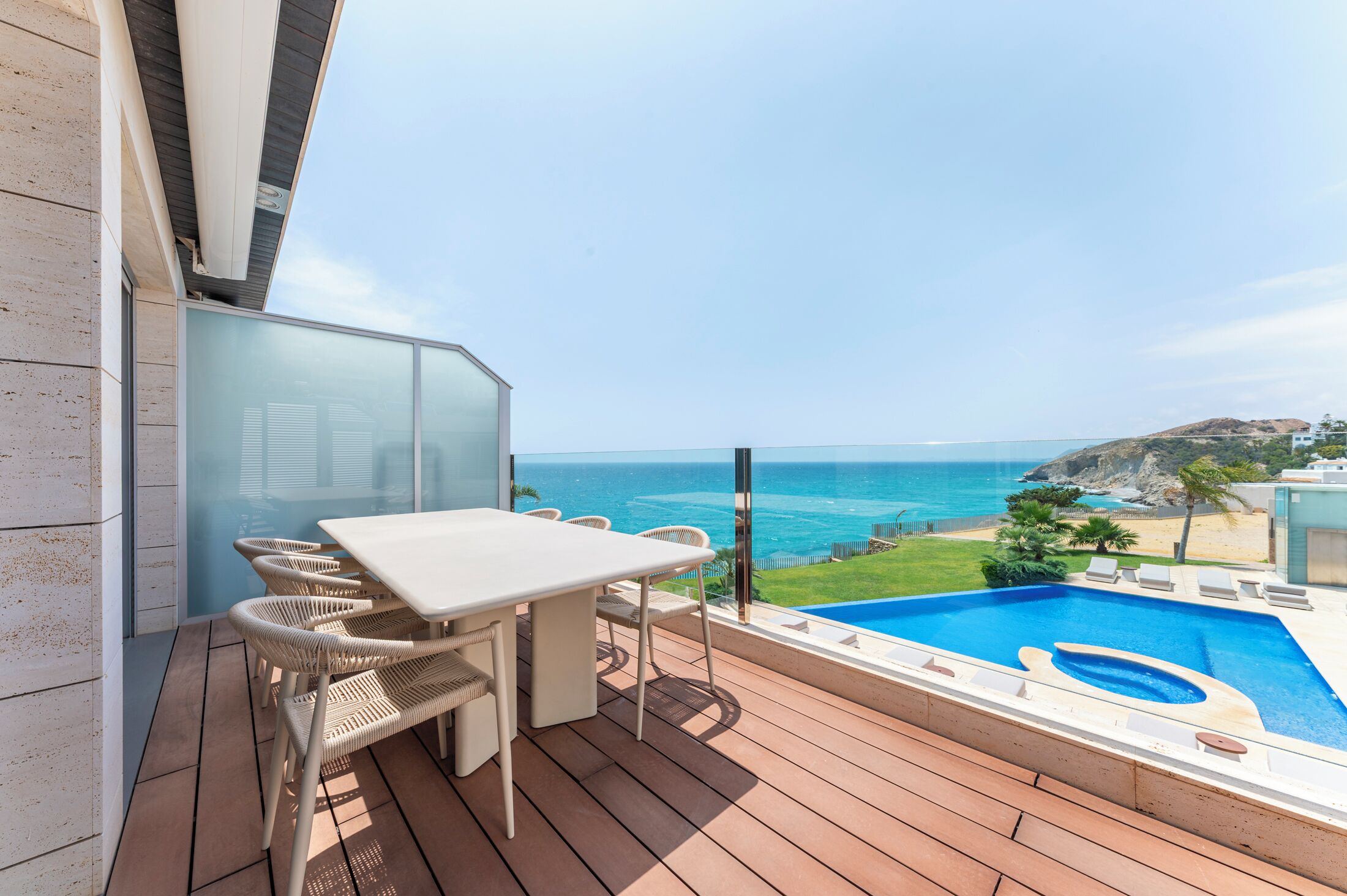 A balcony with a table and chairs, a swimming pool, and a view of the ocean.