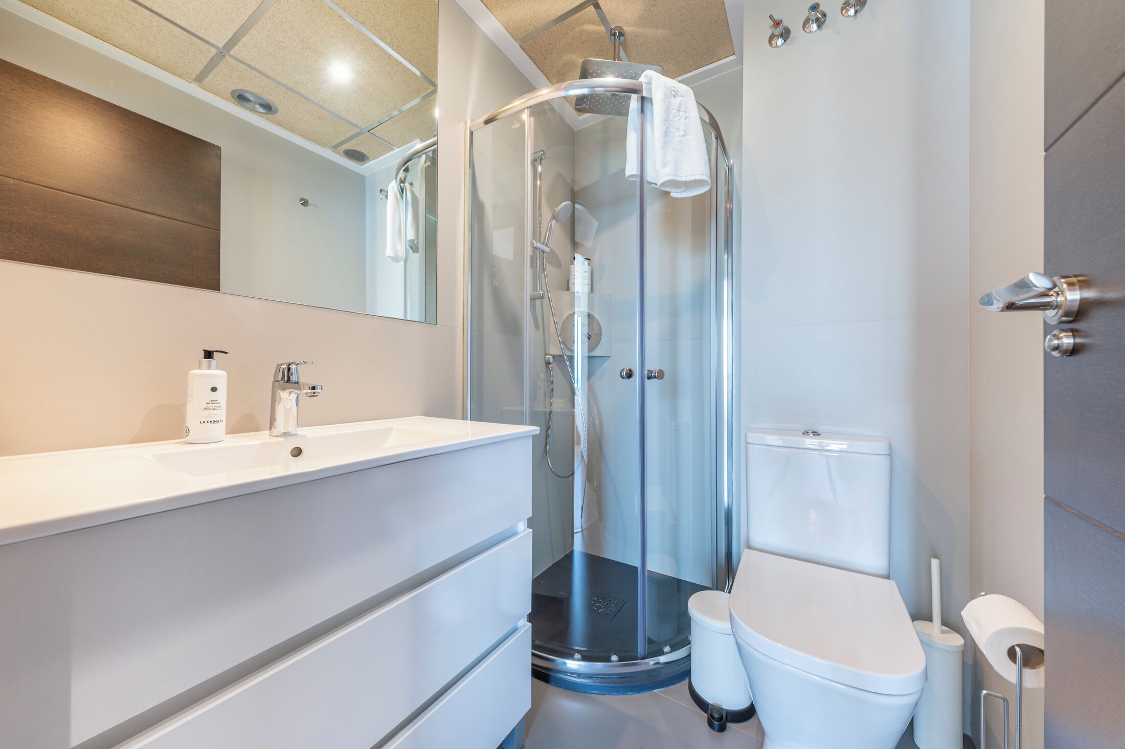 Un baño moderno con ducha envuelta en vidrio, lavamanos blanco y retrete.