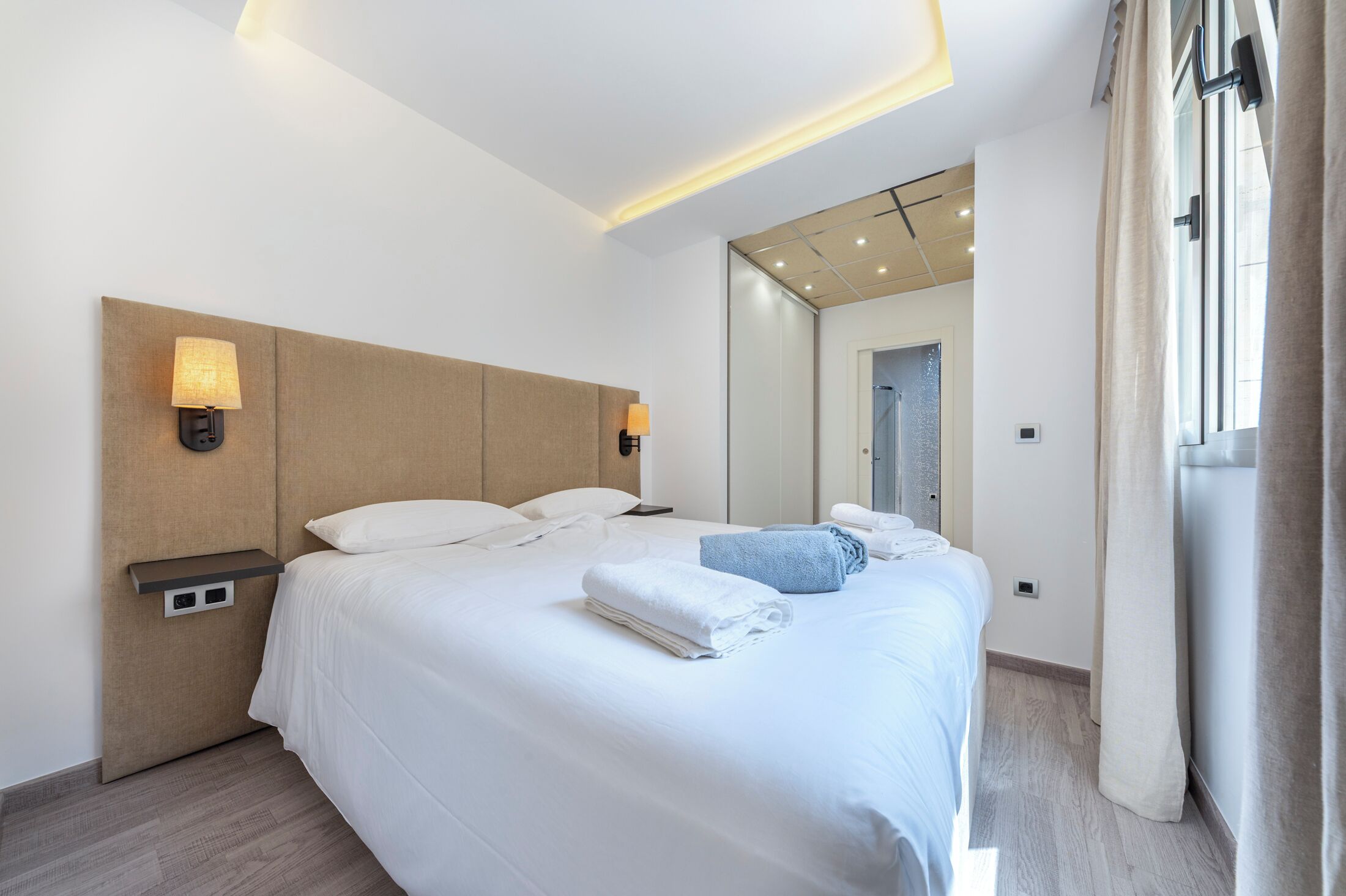 A modern hotel room with a large bed, bedside lamps, a nightstand, and a mirror.