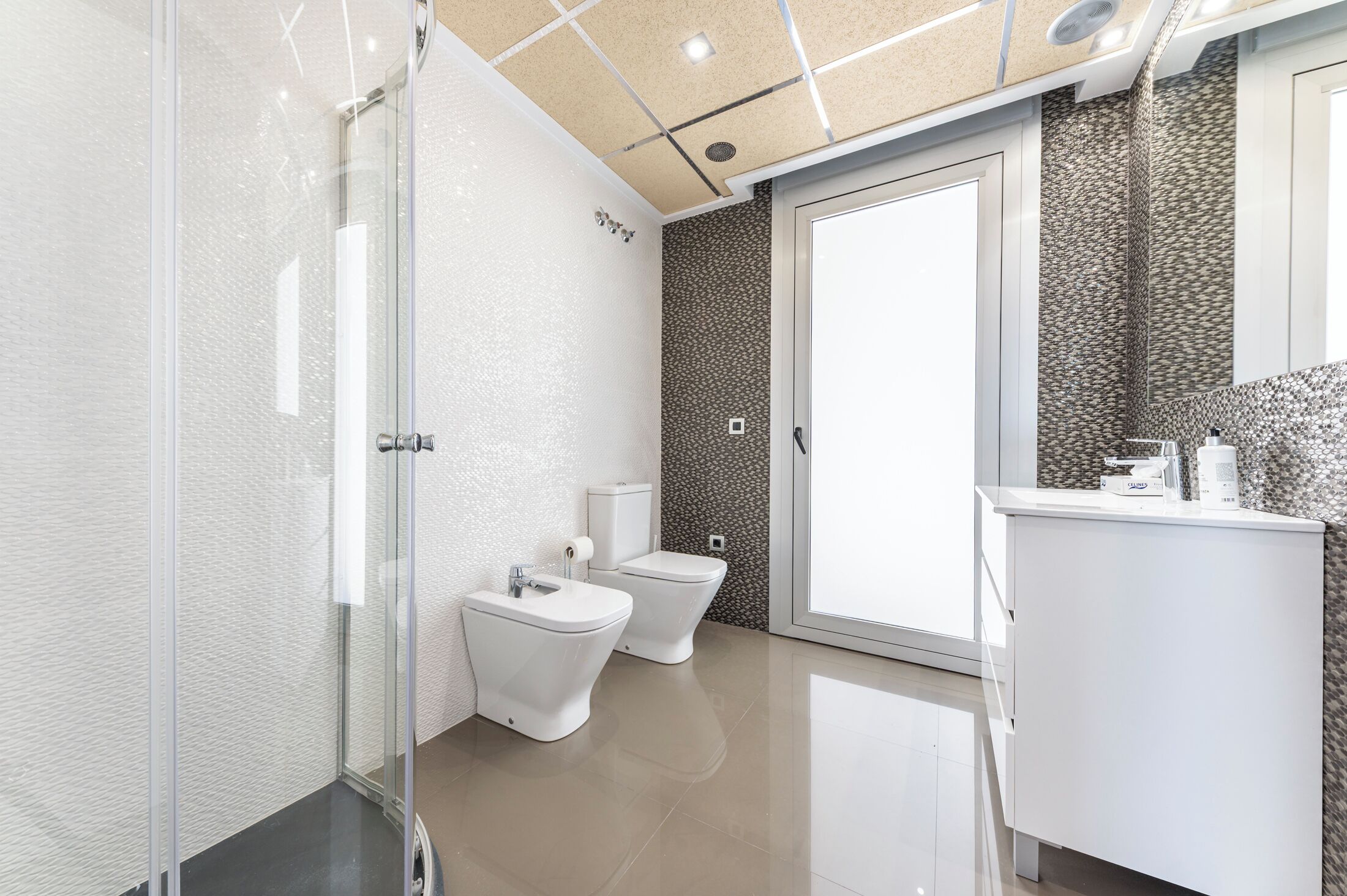 Un baño moderno con cabina de ducha de vidrio, dos inodoros, un lavabo y tocador.