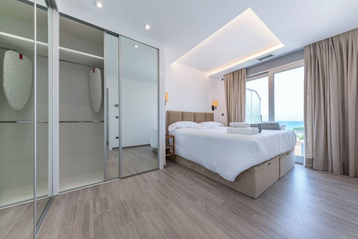 Une chambre d’hôtel moderne avec un grand lit, un placard avec une porte coulissante en verre et une vue sur l’océan.