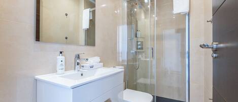 A modern bathroom with a glass-enclosed shower, a white vanity with a mirror, and a toilet.