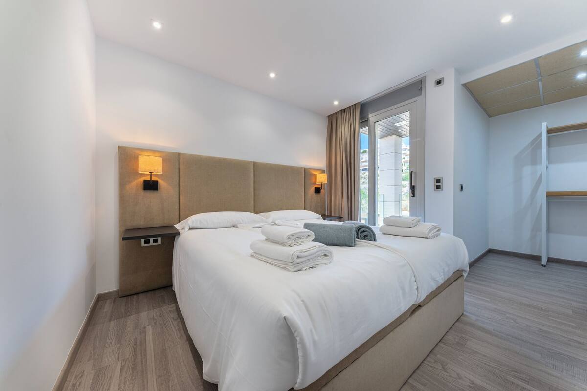 Une chambre d’hôtel moderne dotée d’un grand lit, de deux tables de chevet, d’une étagère intégrée et offrant une vue sur l’extérieur.