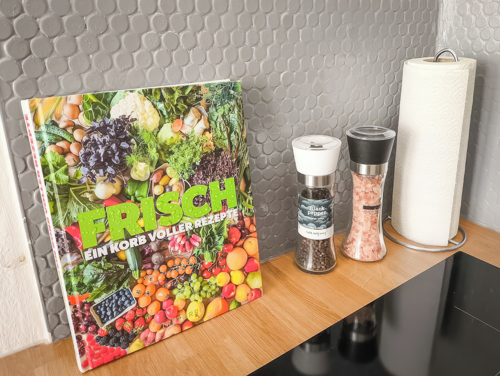 A kitchen counter with a cookbook titled 'Frisch' and two salt and pepper shakers.