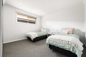 A bedroom with two beds, a window, a nightstand, and a carpeted floor.