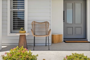 A wicker chair outside a house with a small table and a potted plant.