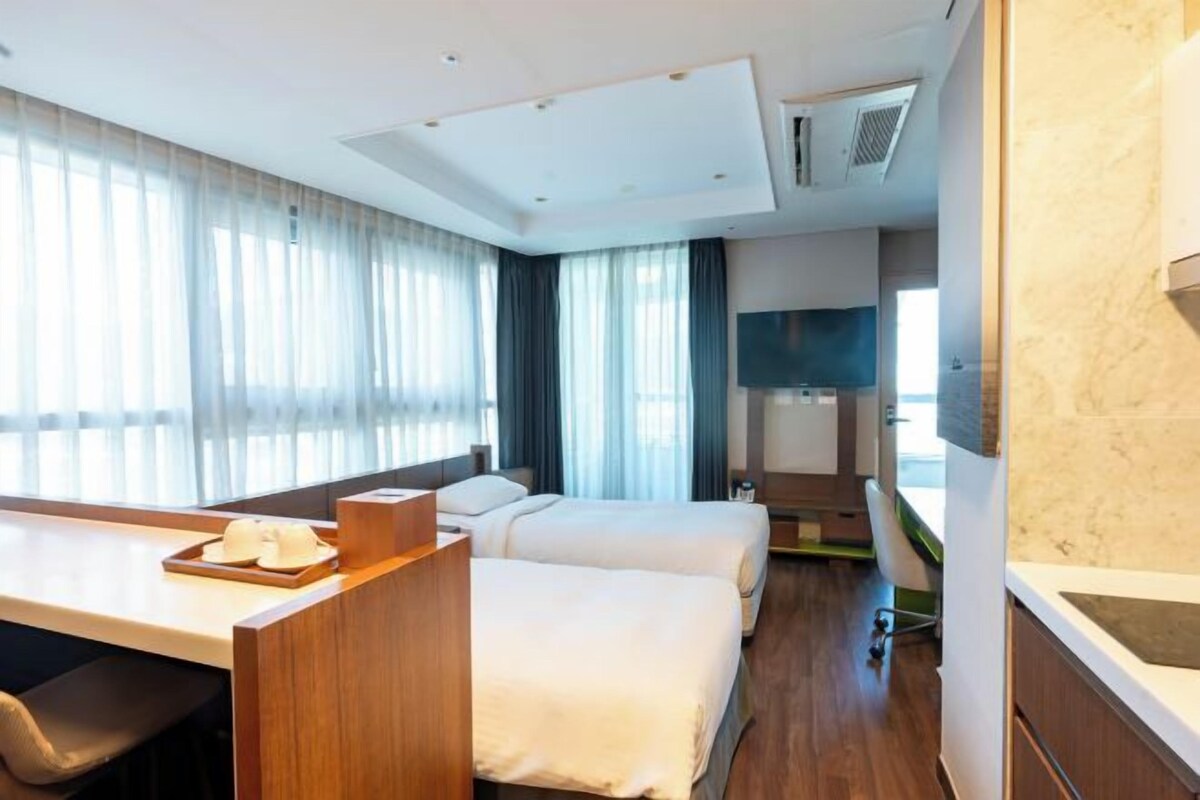 A hotel room with a bed, a desk, a chair, a TV, and a bathroom.