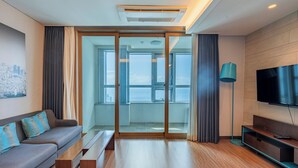 A modern living room with a sofa, a coffee table, a TV, and a sliding glass door leading to a balcony. - hotellamouette (Busan)