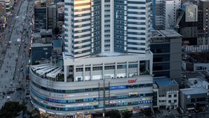 A high-rise building with a curved base, surrounded by other buildings and a busy street. - hotellamouette (Busan)