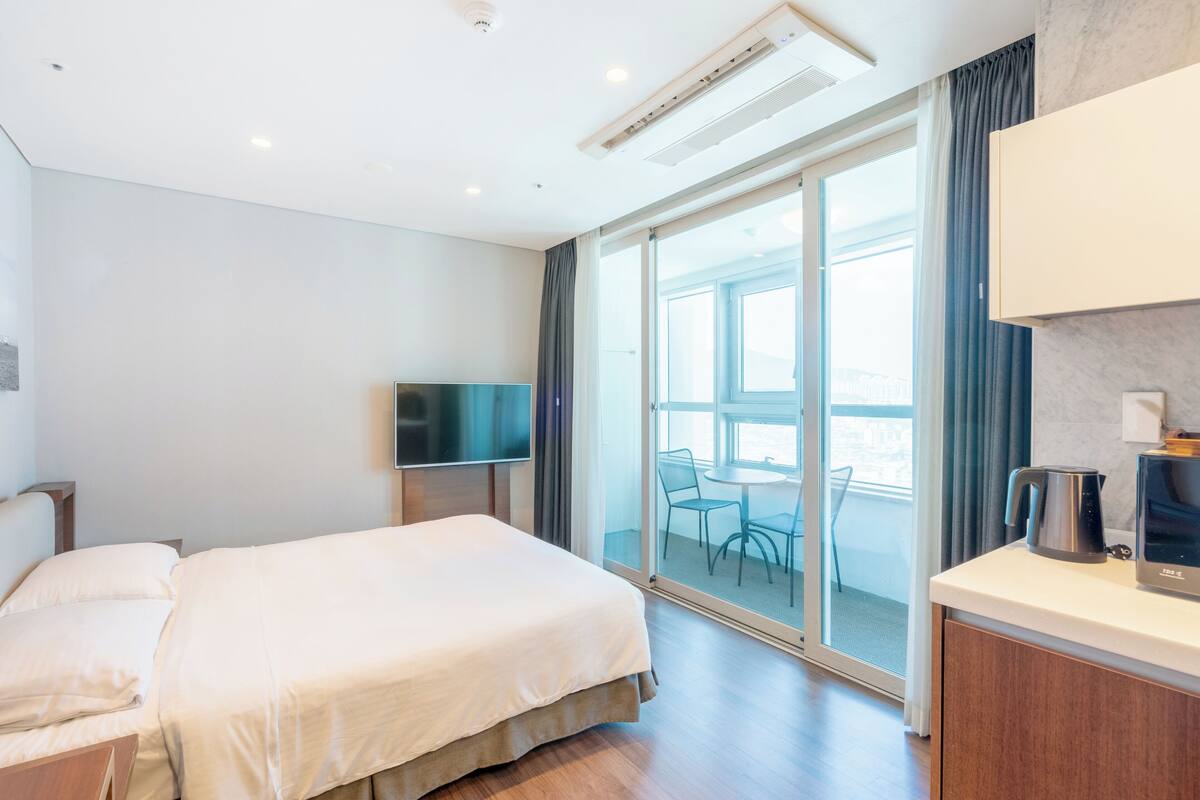 Habitación de hotel con cama, televisor, cafetera y vistas al exterior.